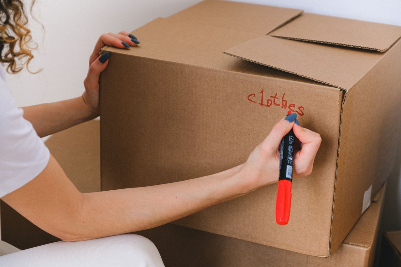 Gros plan d'une femme étiquetant un carton avec un marqueur rouge à l'intérieur.
